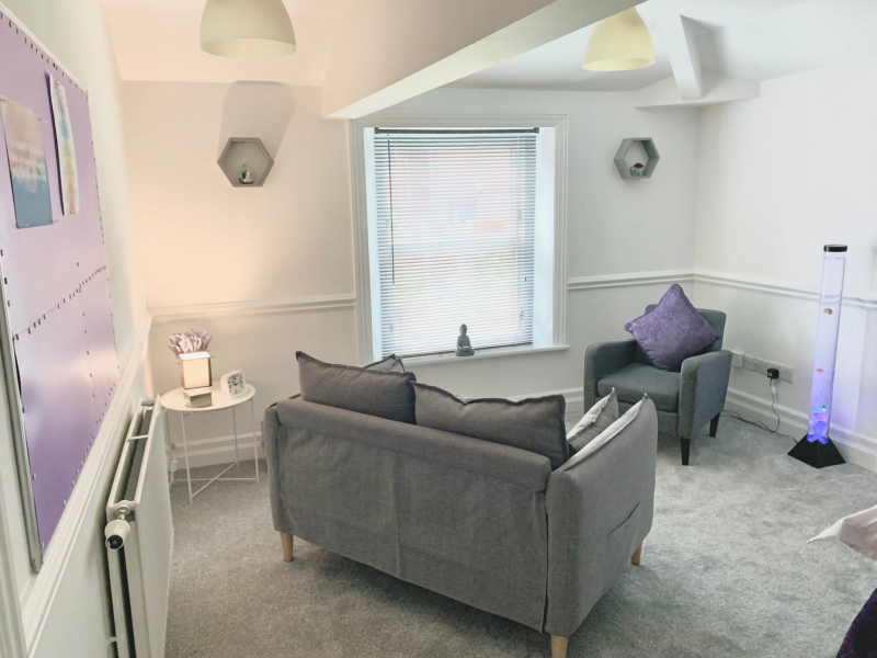 Carolyn's therapy room in Runcorn — a calm, warm counselling space with soft lighting, a comfortable sofa and armchair